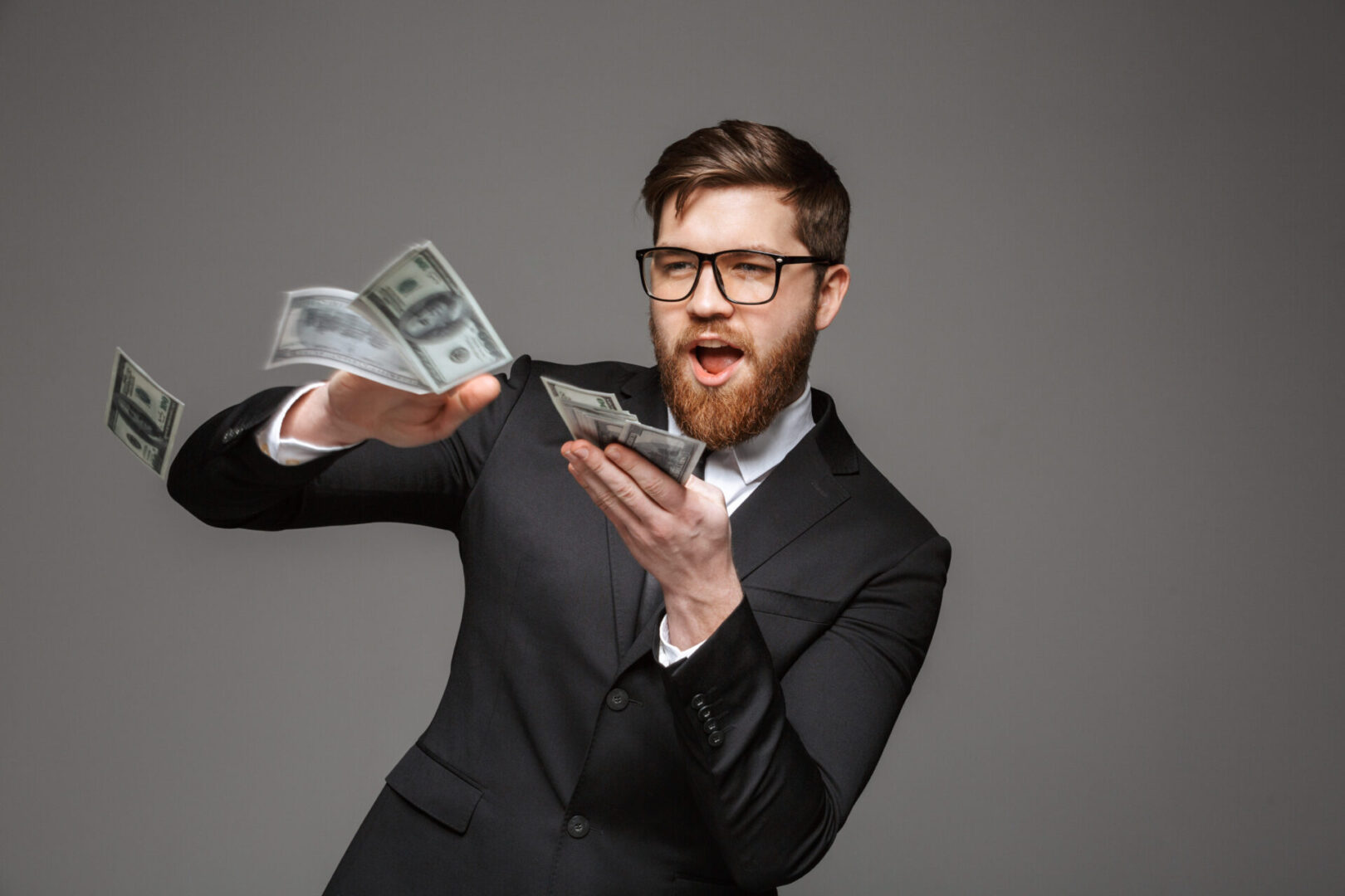 A man in a suit holding money and wearing glasses.